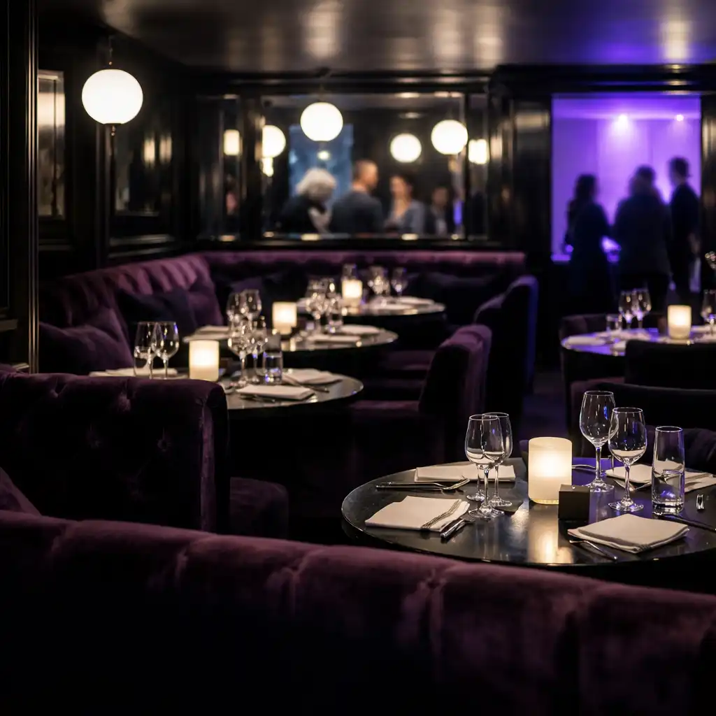 Vue large du salon nocturne de Maison Opaline avec banquettes, tables réelles et silhouettes floues au loin.